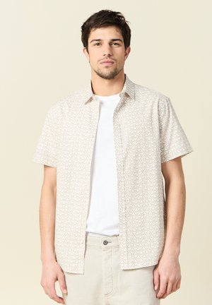 Korte mouwen overhemd met knopen in beige met een geometrisch patroon, gemaakt van lichte stof, met daaronder een wit T-shirt.