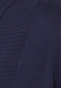 Indumento in maglia di colore blu navy caratterizzato da un design a coste testurizzato e sezioni lisce, che mostrano diversi modelli di lavorazione e sfumature.
