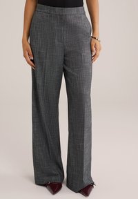 Szürke, bő szárú nadrág texturált, szőtt mintával. Laposhátú derékkal és zsebekkel rendelkezik, burgundi színű, hegyes orrú cipővel párosítva.