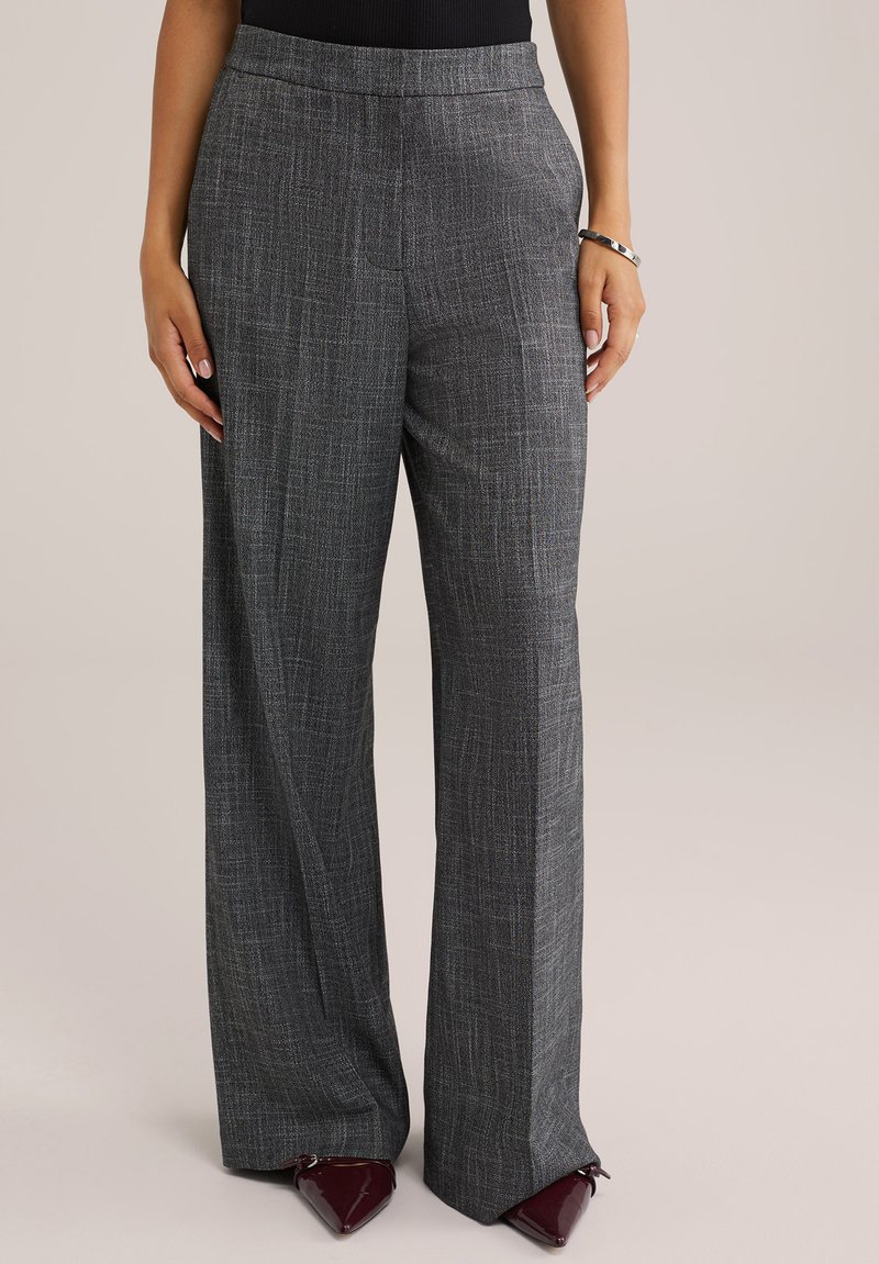 Szürke, bő szárú nadrág texturált, szőtt mintával. Laposhátú derékkal és zsebekkel rendelkezik, burgundi színű, hegyes orrú cipővel párosítva.