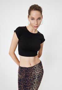 Schwarzes, kurzärmeliges, cropped T-Shirt, kombiniert mit einem figurbetonten Rock im Leopardenmuster. Glatte Textur, schlichtes Design, anatomische Passform.