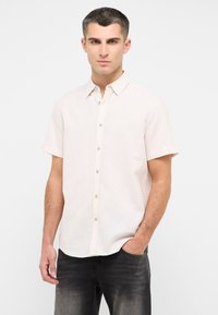 Krótka, jasnoróżowa koszula na guziki z kołnierzykiem, subtelną teksturą i jasnobrązowymi guzikami, zestawiona z ciemnoszarymi dżinsami.