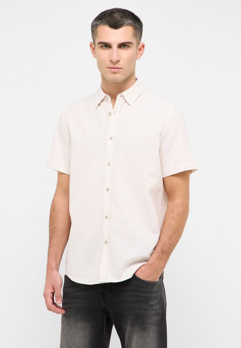 Krótka, jasnoróżowa koszula na guziki z kołnierzykiem, subtelną teksturą i jasnobrązowymi guzikami, zestawiona z ciemnoszarymi dżinsami.