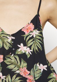 Černé květinové šaty se živými růžovými a zelenými tropickými vzory, nastavitelné špagetové ramínka a detail knoflíku na výstřihu.