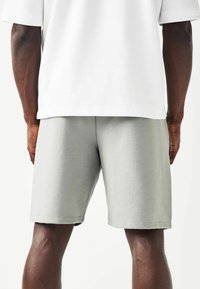 Shorts en coton gris clair avec une coupe décontractée, présentant une texture lisse et une taille élastique. Le modèle porte un t-shirt oversized blanc.