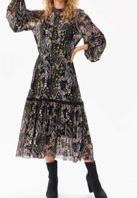 Robe noire transparente avec motif paisley en nuances de bleu, rose et or ; manches longues bouffantes et jupe à volants à étages avec accents volantés.
