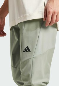 Jasnozielone spodnie sportowe z teksturowanym wykończeniem, z czarnym logo Adidas z boku i dopasowanym krojem zapewniającym komfort i swobodę ruchów.