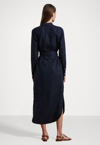 Dark blue linen shirt dress with a belted waist, long sleeves, and a slit at the hem. Features a collared neckline and buttoned cuffs.