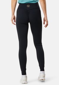 Leggings noirs avec une taille haute et une couture centrale froncée à l'arrière. Texture lisse, associés à des chaussures de sport blanches.