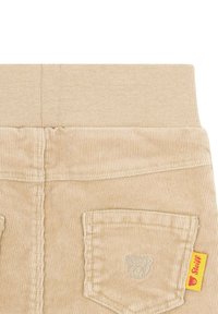 Béžové manšestrové kalhoty s elastickým pasem, se malým emblémem medvěda na zadní kapse a žlutou značkovou etiketou na boku.