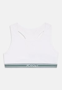 Sutiã desportivo branco em algodão com design nas costas em formato de corredor, apresentando uma faixa horizontal verde e branca e o logótipo "LACOSTE" na parte inferior.