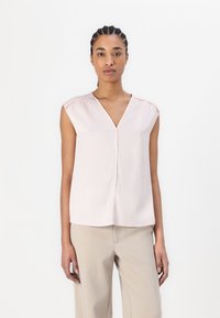 Blusa senza maniche rosa chiaro con scollo a V, texture liscia e cuciture decorative sulle spalle. Abbinata a pantaloni beige.