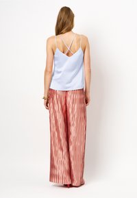 Lichtblauw mouwloos top met een crisscross rugontwerp, gecombineerd met roségouden geplooide wijde pantalon met een glanzende textuur.