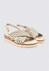 Sandalias tejidas con un diseño de tira cruzada en dorado y beige, que presentan una parte superior con patrón y una suela texturada de color claro.
