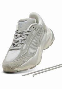 Sneaker grigio con una tomaia in suede texturizzato, pannelli in mesh e suola in gomma. Presenta lacci piatti e un design curvo con un colletto imbottito.