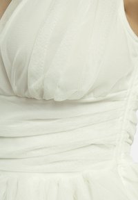 Robe blanche en tulle transparent, avec un corsage froncé, une texture douce et une jupe superposée avec un ourlet volé.