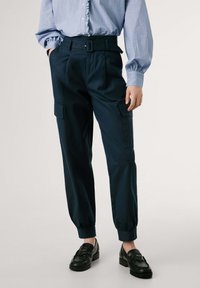 Marinblå cargobyxor med bälte vid hög midja, som har sidofickor, avsmalnande anklar och ett mjukt, lätt tyg. I kombination med svarta loafers.
