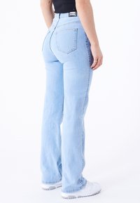 Light blue denim flared jeans with a high rise, featuring back pockets and a slight fade. Paired with white sneakers.