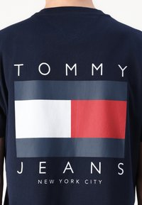 Navyblaue Baumwoll-T-Shirt mit einem großen grafischen Druck, der ein rechteckiges Logo in Rot, Weiß und Blau zeigt. Der Text lautet "TOMMY JEANS NEW YORK CITY."