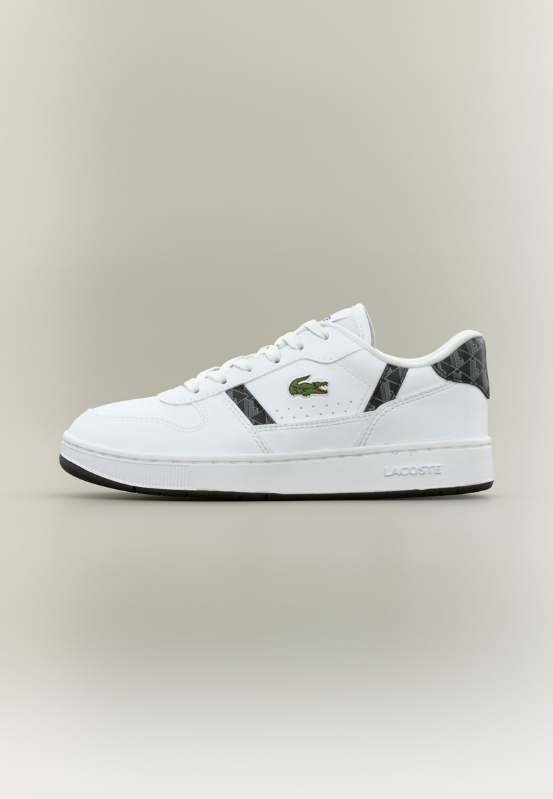 Λευκό αθλητικό παπούτσι Lacoste με μαύρες γεωμετρικές λεπτομέρειες, πράσινο λογότυπο κροκοδείλου στο πλάι και λευκή σόλα με την εγχάρακτη λέξη "Lacoste" στην φτέρνα.