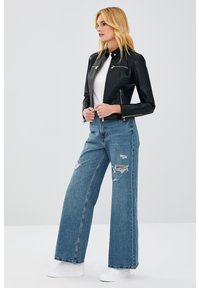 Black faux leather jacket with zippers, paired with distressed wide-leg blue jeans and white sneakers, featuring a smooth texture.