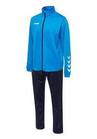 Jas en broekset in helder blauw en marineblauw. De jas heeft een hoge kraag, een rits aan de voorkant en witte chevrondetails op de mouwen. Soepele stof.