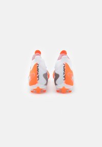 Ghete de fotbal albe cu accente portocalii, având un upper texturat, crampoane modelate și brandingul "ULTRAX" pe călcâi.