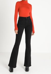 Röd långärmad polotröja som kombineras med högmidjade svarta bootcut-jeans, med en slät yta och en åtsittande design.