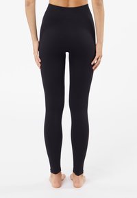 Svarta ribbade leggings med hög midja, med en slät yta och figursydd silhuett, sträcker sig från midjan till anklarna.