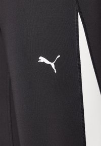 Svarta träningsleggings i slät tyg, med en vit Puma-logotyp och en kontrasterande vit panel på sidan med sydda detaljer.