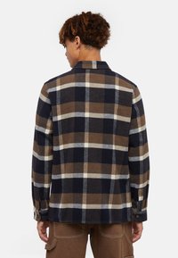 Brun og marineblå plaid flannel skjorte med lange ærmer, knapmanchetter og rygdetalje. Blød tekstur og struktureret design.