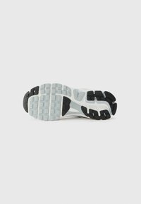 Semelle de sneaker blanche et noire avec un motif de grip texturé, présentant une forme courbée et des zones renforcées pour la durabilité.