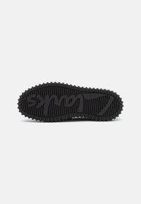 Sole di sneaker nera con texture a coste, con il nome del marchio prominentemente impresso al centro. Righe circolari lungo il bordo per una migliore aderenza.