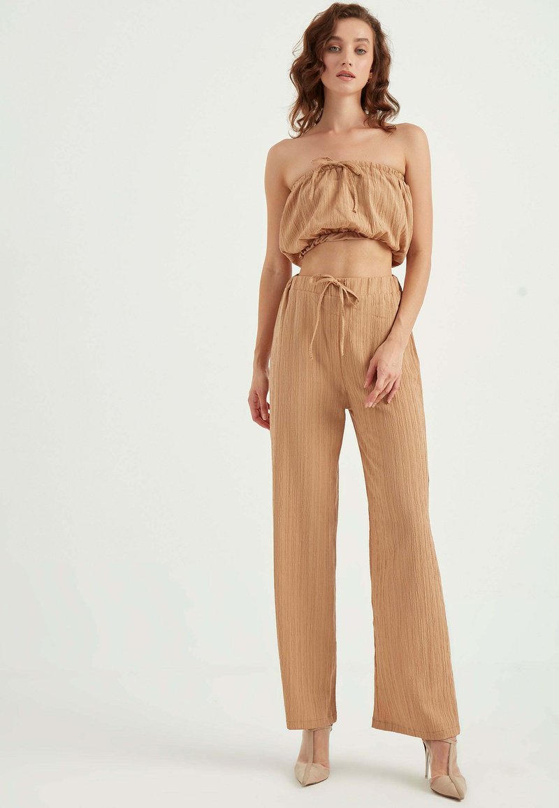 Beżowy, dwuczęściowy zestaw składający się z strapless, krótkiego topu o marszczonej fakturze oraz spodni z wysokim stanem i szerokimi nogawkami z detalem w postaci wiązania.