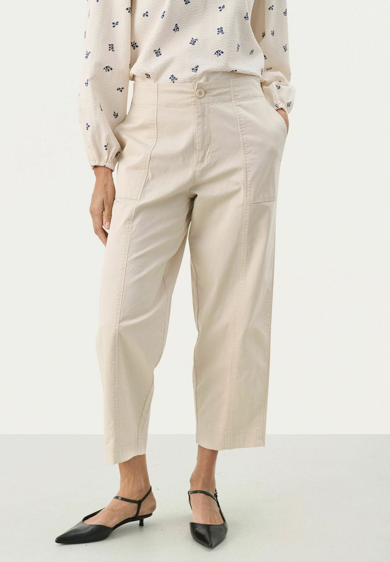 Beige cropped broek met een ontspannen pasvorm, zijzakken en zichtbare stiksels. Gecombineerd met zwarte pumps met een spitse teen.