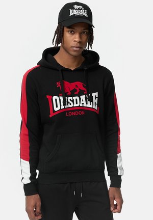 Sudadera negra con rayas laterales rojas y blancas, con un gráfico de león y el texto "Lonsdale London". Fabricada en algodón y con un bolsillo frontal.