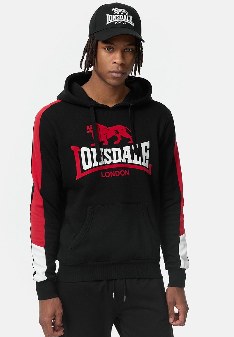 Sudadera negra con rayas laterales rojas y blancas, con un gráfico de león y el texto "Lonsdale London". Fabricada en algodón y con un bolsillo frontal.