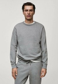 Sudadera griș cu guler rotund, manșete ribelate și croială lejeră. Asortată cu pantaloni de trening gri, cu detalii albe la șnur.