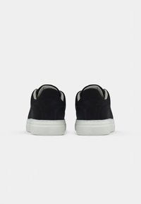 Et par svarte sneakers med hvite såler vist bakfra mot en enkel hvit bakgrunn.