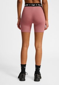 Aangestrikte, roze sportshorts met een zwarte logo tailleband, gecombineerd met zwarte sportsokken en schoenen, die een gladde, rekbare stof laten zien.