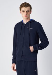 Felpa con zip color blu navy realizzata in materiale morbido, con tasca frontale, cordini e logo sul petto.