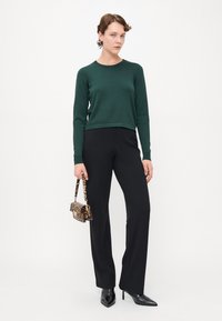 Pull vert à manches longues, pantalon noir ajusté et escarpins noirs à bout pointu. Petit sac à main imprimé léopard avec une courte anse.