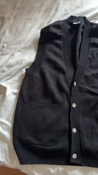 Schwarze ärmellose Strickjacke mit strukturierter Rippoptik, V-Ausschnitt, sechs Knöpfen und zwei Vorderentaschen.