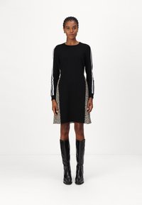 Schwarzes Kleid mit langen Ärmeln und Leopardenmuster an den Seiten. Mit weißen Streifen an den Ärmeln. Schwarze kniehohe Stiefel runden den Look ab.