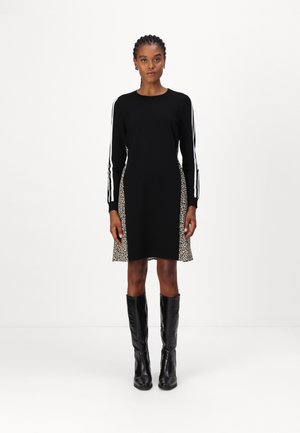 Schwarzes Kleid mit langen Ärmeln und Leopardenmuster an den Seiten. Mit weißen Streifen an den Ärmeln. Schwarze kniehohe Stiefel runden den Look ab.