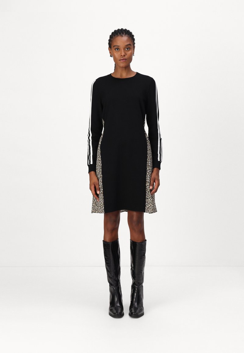 Schwarzes Kleid mit langen Ärmeln und Leopardenmuster an den Seiten. Mit weißen Streifen an den Ärmeln. Schwarze kniehohe Stiefel runden den Look ab.