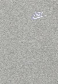 Šedé bavlněné tričko s texturovanou látkou. Na horní levé straně je vyšitý malý fialový logotyp Nike.