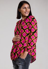 Bunte Bluse mit einem geometrischen Muster aus pinken und gelben Quadraten auf schwarzem Hintergrund, mit langen Ärmeln und lockerer Passform.