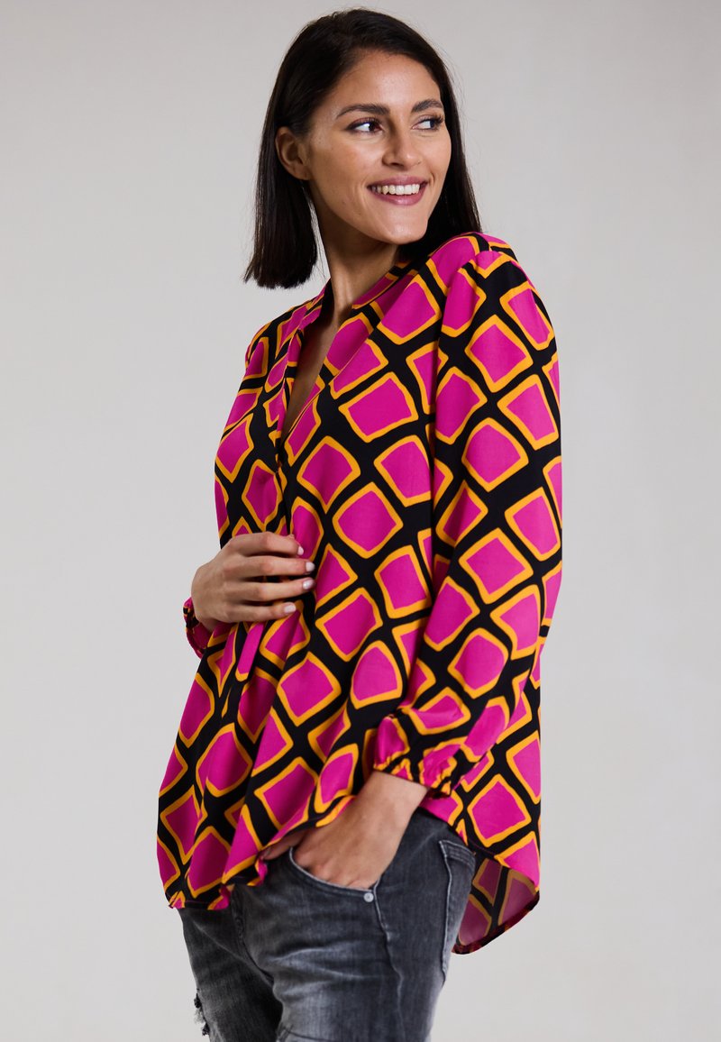 Bunte Bluse mit einem geometrischen Muster aus pinken und gelben Quadraten auf schwarzem Hintergrund, mit langen Ärmeln und lockerer Passform.
