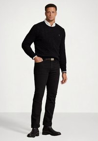 Μαύρο πουλόβερ με πλέξη καλτσοδέτας πάνω από ένα λευκό πουκάμισο με γιακά, σετ με μαύρα τζιν και μαύρα μποτάκια. Απλός σχεδιασμός, μονόχρωμα και εφαρμοστή γραμμή.